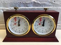 Front view of the dual dial chess clock with visible BHB branding on clock faces and brass knobs on top.