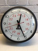 Front view of Edwards round wall clock showing white face with black and red 24-hour numbering, black frame, and clock hands at approximately 12:25:43.
