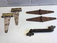 Photo showing all items: two T-hinges and a coil spring door closer, placed on a white surface.