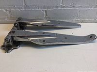 Side view of two large antique fridge hinges showing length and shape with bends in hinge arms