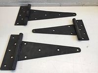 Three black metal T-hinges arranged on white surface, showing their sizes and mounting holes.