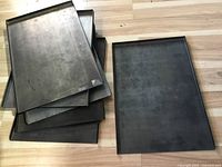 Photo showing six stacked metal trays with flat base and three raised edges, showing general condition and quantity.