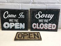 Three hand painted open/closed signs with distinct sizes and styles shown together on a white background with brick wall behind.