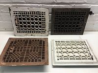 Four metal air vents laid out together. Includes a rusty brown vent on bottom left, two matching vents (white one on bottom right, black one top right), and a weathered white vent top left.