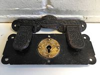 Close-up of Victorian trunk closure latch showing embossed ornate pattern and dual latch tabs
