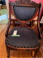 Front view of the antique chair showing carved wood top and riveted dark fabric upholstery on backrest and seat.