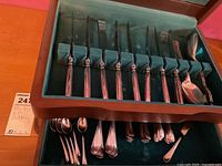 Photo showing the open wooden storage box with green felt lining holding an assortment of Birks plated flatware including knives, forks, spoons and serving utensils arranged in compartments.