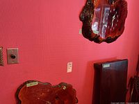 Two large burl wood wall clocks displayed on a red wall, showing their natural shape and reddish polished finish.