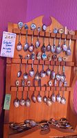 Full view of collectible spoons on wooden rack against purple textured wall with MaxSold tag.