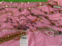 Overview of the costume jewelry laid out on pink fabric, showing multiple necklaces of various styles, beads, and pendants.