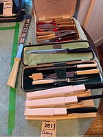 Image showing a large saw blade with cream handle, a set of eight vintage knives with wooden handles in a fitted box, carving knife and fork with silver and cream handles in a green velvet-lined case