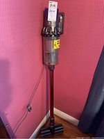 Full assembled vacuum standing on charger with cord plugged into wall