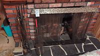 Fireplace tools and screen set up in front of brick fireplace, set includes tools in stand and screen.