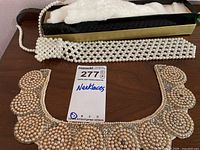 Full view of the pearl necktie necklace alongside the vintage hand-stitched collar accent displayed on a wooden surface with the lot tag.
