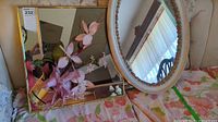 Two mirrors, one rectangular with gold frame and one oval with floral painted white frame, placed on a floral fabric surface