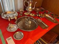 Full display of silver-tone serveware set featuring coffee pot, trays, salt and pepper shakers, and side dishes on red cloth.