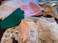 Photo showing folded assorted vintage table linens and napkins in various colors and patterns, including pink, green, lace, and crochet pieces.