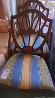 Photo showing two vintage wood chairs with upholstered seats in striped fabric under natural light.
