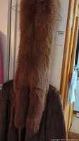 Photo showing a long brown fur stole hanging against the wall with part of the brown fur jacket visible underneath.