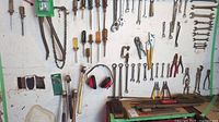 Wide view showing wall-mounted wrenches, screwdrivers, pliers, pipe wrench, clamp, hammer, wire brush and earmuffs lying on bench