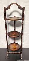 Front view of the antique wooden pie/cake stand showing three round tiers and carved handle top.