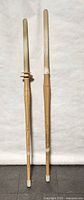 Photo showing two bamboo wood practice swords side by side against a white background, details of bamboo segments and white wrapped handle ends visible.