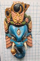 Close-up of the blue wooden Ganesh head face mask showing the paint and decorative details with measurement grid background indicating approximately 9 inches height.