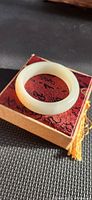 Top view of pale greenish white jade bangle resting on red patterned fabric box