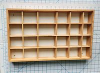 Top-down view of the wood curio shelf showing the rectangular frame and 21 square compartments, placed on a cutting mat with measurement grid for scale.