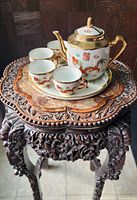 Photo showing complete tea set including teapot, tray and four cups placed on ornately carved wooden table.