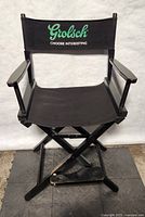 Front view of black folding directors chair with green Grolsch branding on backrest, wood armrests, and fabric seat.