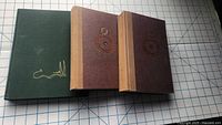 Front view of three hardcover Tolkien books showing two brown 1993 Lord of the Rings editions and one green 1997 Hobbit edition.