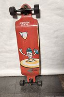 Full top view of red Landyachtz longboard with character graphic and black wheels on white background.