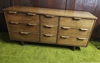 Front view of nine-drawer walnut dresser on green carpet against wood panel wall