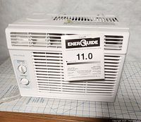 Front view of Insignia window air conditioner showing control panel, grille, and EnerGuide label with 11.0 energy rating.