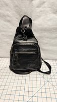 Front view of a small black leather backpack with zippered front pocket and top clip