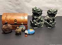 Full lot of five snuff bottles, two carved green hardstone Foo Dogs, and wooden box with carved top shown together on black surface.