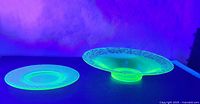Both large dish and small plate glowing under UV light showing the uranium glass characteristic fluorescence.