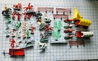 Overview photo of vintage Western themed plastic toy figures and accessories laid out on a grid background including people, horses, carriages, a teepee, trees, fences, and a canoe.