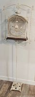 Full height view showing cage hanging on tall wrought iron stand with square base