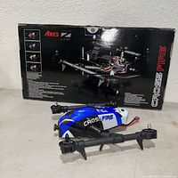Ares Z-Line Crossfire quadcopter drone in front of its original packaging box labeled with branding and specs.