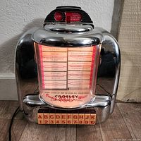 Front view showing the jukebox style song selection panel with lettered and numbered buttons and coin slot instructions