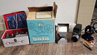 Wide shot of all items included showing the microscope in the open case, Baia movie editor box and accessories, Sears camera, and small tools spread on floor.