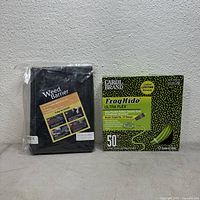 Front view of black woven weed barrier fabric in plastic packaging and Carol Brand FrogHide Ultra Flex 50 ft power cord box with green and black design.