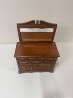 Front view of wooden jewelry box with closed drawers, hinged top with mirror.
