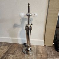 Chrome Mid Century Atomic Age style table lamp standing on wood floor against white wall, unlit.