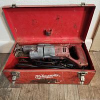 Open red Milwaukee metal toolbox with reciprocating saw and blades inside