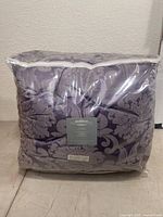 Front view of the packaged purple damask patterned comforter set in clear plastic bag showing compact packaging.