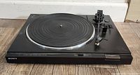 Black Sony PS-LX220 automatic belt-drive stereo turntable on wood floor, showing front and side controls.