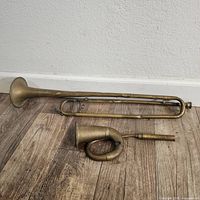 Full view of both items showing bugle and curved car horn on wood floor with visible dents and tarnish.